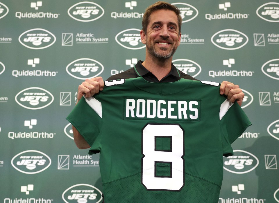 Aaron Rodgers holding up his new New York Jets jersey.