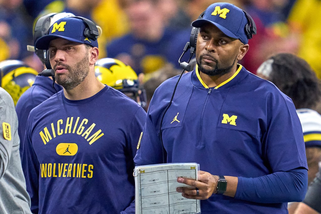Two Michigan Wolverines football coaches on the sidelines.