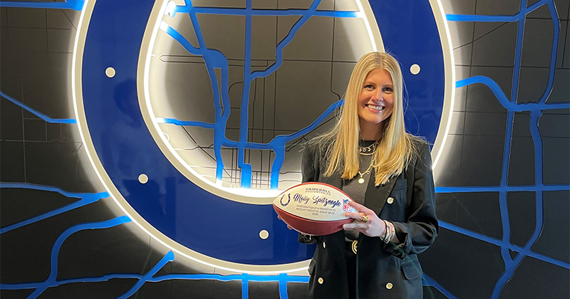 Molly Spitznogle holds a football and stands in front of a big sign featuring the Indianapolis Colts logo.