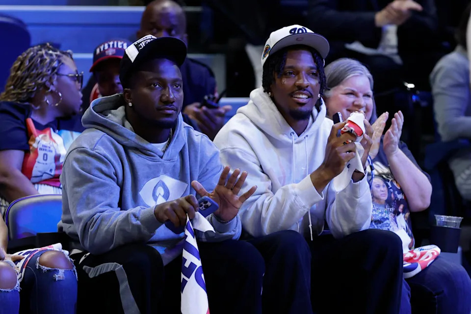 Washington, District of Columbia, USA; Washington Commanders wide receiver Deebo Samuels (L) and Commanders quarterback Jayden Daniels (R) wave to the crowd from courts wide during the game between the Washington Mystics and Atlanta Dream at CareFirst Arena. Geoff Burke-Imagn Images