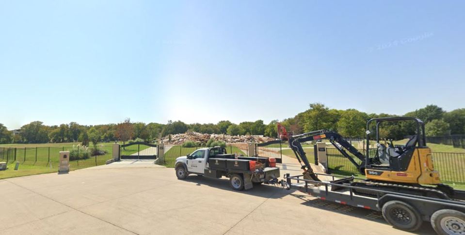 Demolition debris behind a gated entrance with a pickup truck and a small excavator.