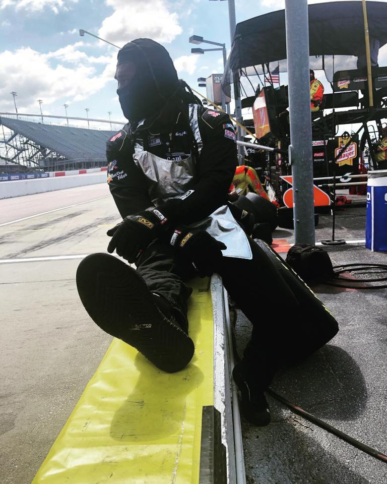 NASCAR mechanic sitting on a wall at a racetrack.