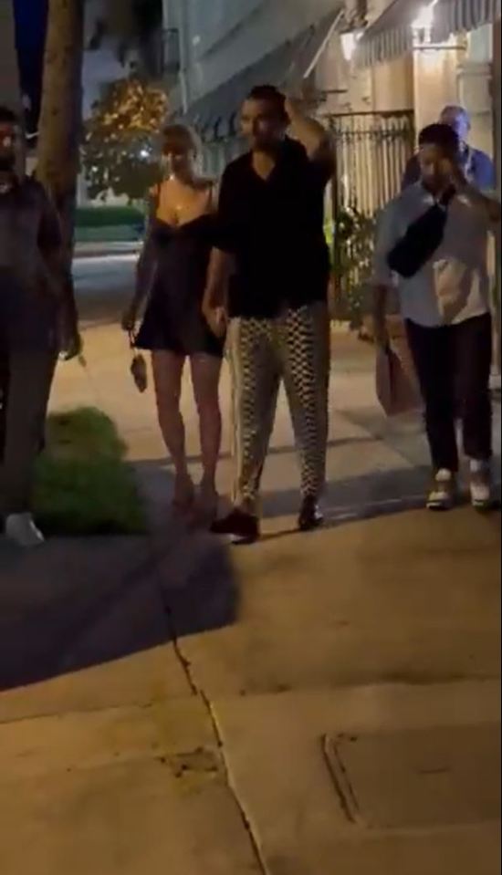 Taylor Swift and Travis Kelce walking down a street at night.