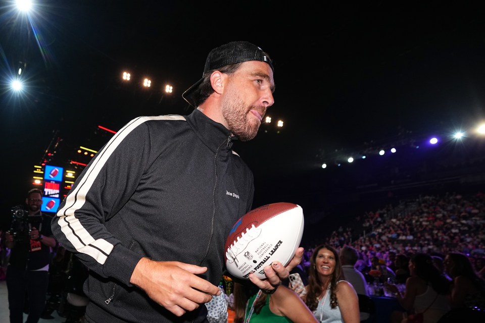 Travis Kelce holding a football at a celebrity event.