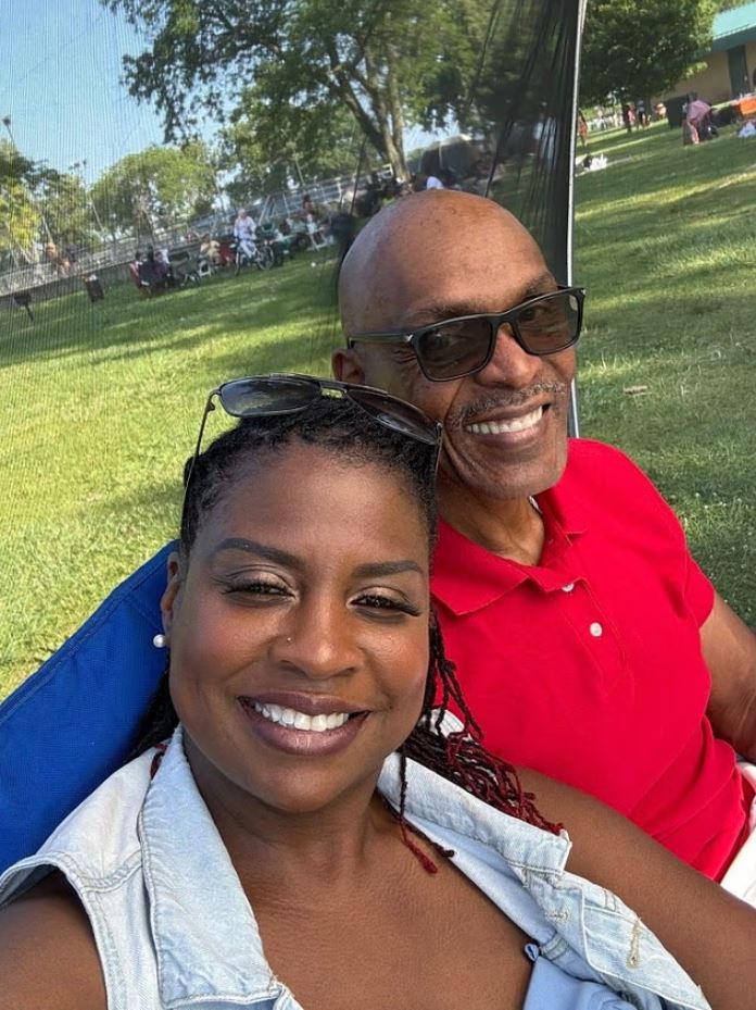 A man and woman smiling for a selfie outdoors.