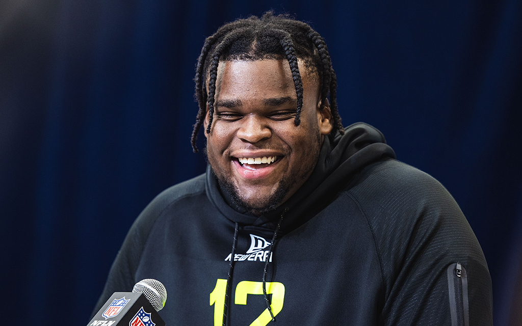 Person smiling in a black hoodie with a microphone bearing an NFL logo.