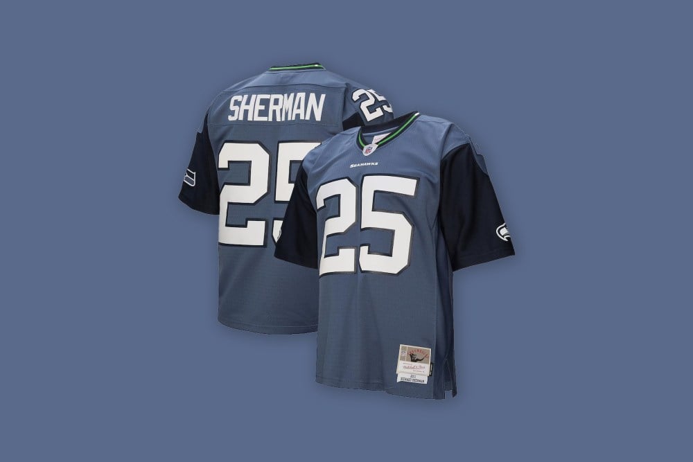 Front and back views of the Richard Sherman Seattle Seahawks Mitchell & Ness 2011 Legacy Jersey in blue against a light blue background.