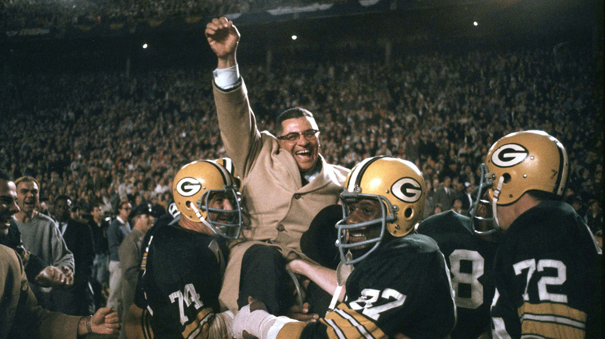Green Bay Packers head coach Vince Lombardi celebrates as he is carried off the field by defensive tackle (74) Henry Jordan and defensive end (87) Willie Davis after the Packers beat the Dallas Cowboys 34-27 during the 1966 NFL Championship Game at the Cotton Bowl. 