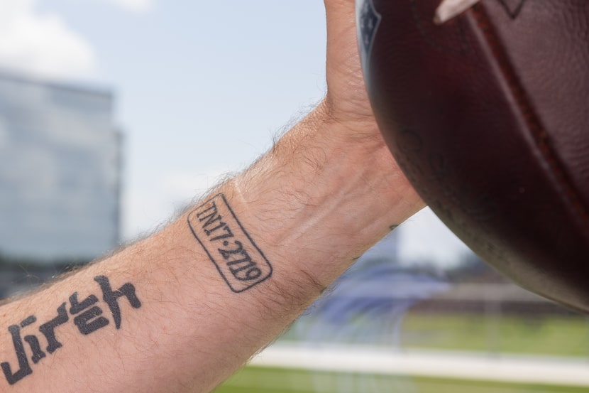 Dallas Cowboys coach Brian Schottenheimer holds a football as he shows off his arm tattoos...