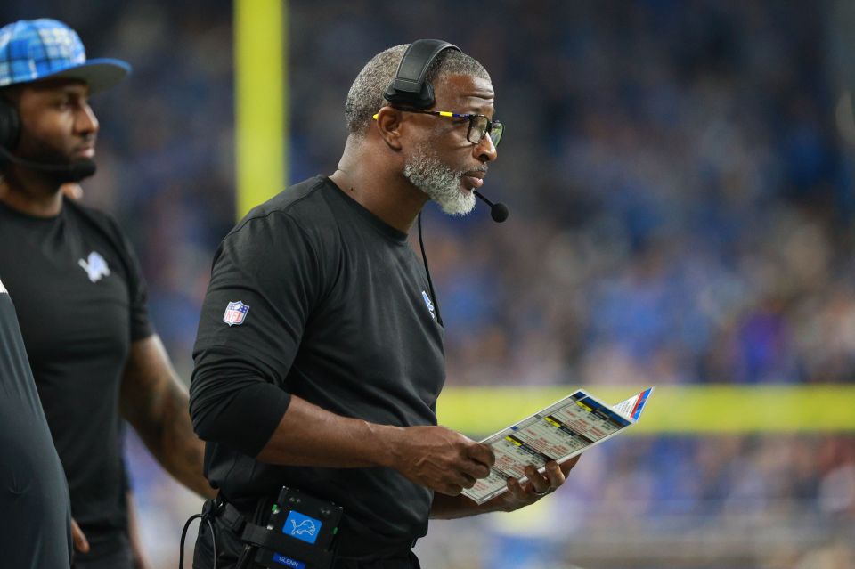 Aaron Glenn, Detroit Lions defensive coordinator, on the sidelines reviewing a playbook.