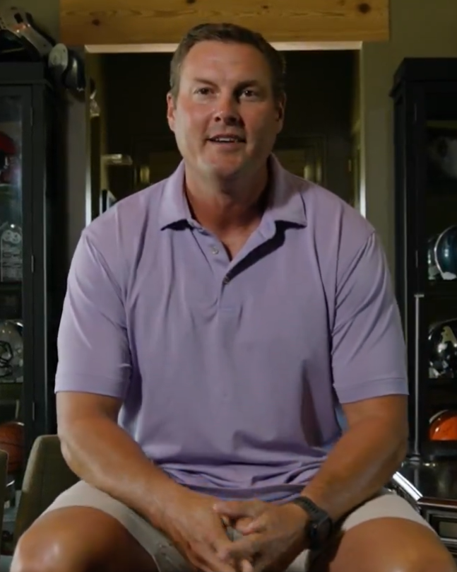 Man in purple polo shirt sitting and talking.