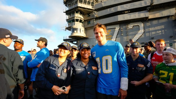 Crew members from the USS Abraham Lincoln (CVN 72), take photos with Los Angeles Chargers quarterback Justin Herbert on the flight deck. (Nelvin C. Cepeda / The San Diego Union-Tribune)