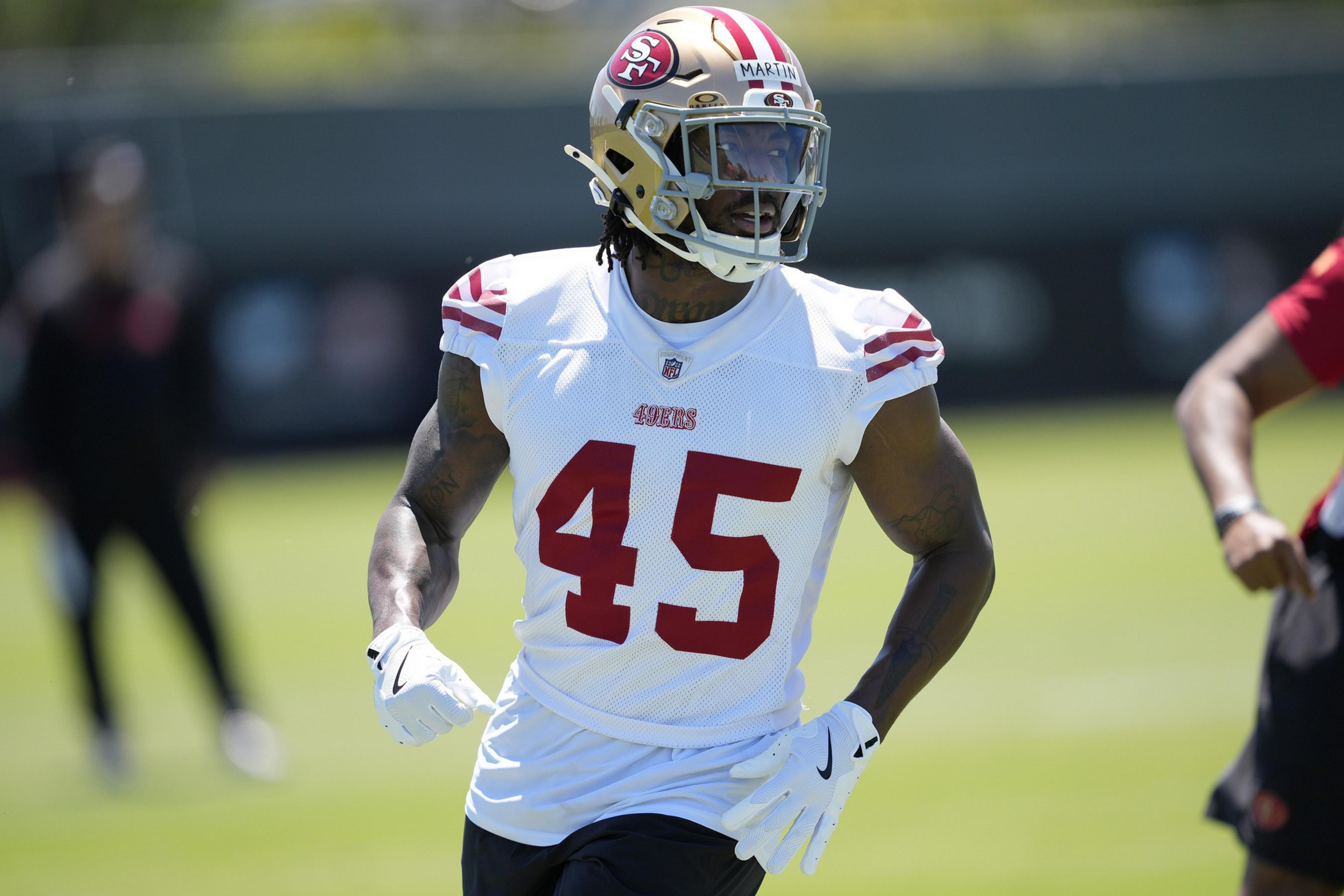 A football player wearing a 49ers jersey with the number 45 is on a field. He has on a gold helmet and white gloves, and the background is blurred.