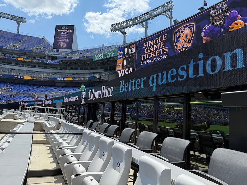 Two rows of nice field-level seats at a football stadium, with signs and other standard seats of the two seating bowls in the background.