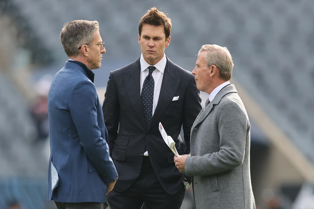 Three men in suits talking at a football game.