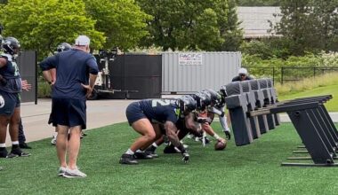 New Seahawks line coach John Benton (left in white cap), a veteran of 19 NFL seasons coaching, works right tackle Abe Lucas (72, center foreground) and the starting offensive line through a sled drill during organized team activities (OTAs) offseason practices June 4, 2025, at the Virginia Mason Athletic Center in Renton.