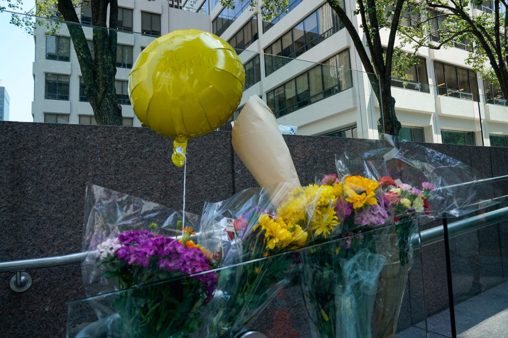 Flowers and a balloon reading "Love one another" are left outside the 345 Park Avenue building