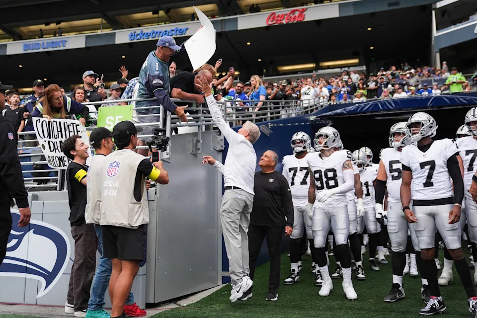 Las Vegas Raiders head coach Pete Carroll, center, tries to grab a sign that reads 