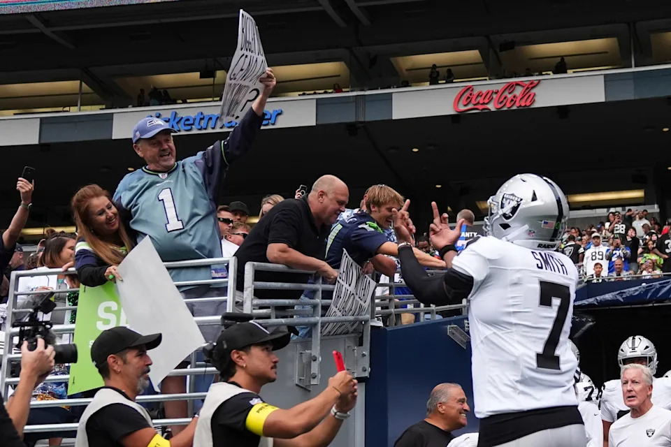 Las Vegas Raiders quarterback Geno Smith gestures to a Seattle Seahawks fan holding a sign before an NFL preseason football game Thursday, Aug. 7, 2025, in Seattle. (AP Photo/Lindsey Wasson)