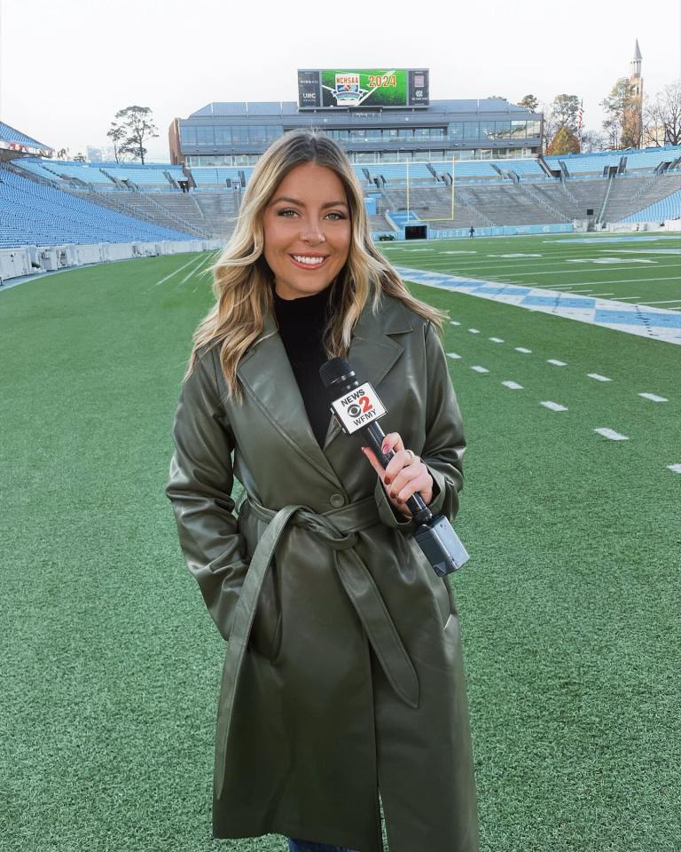 Reporter holding microphone in front of football stadium.