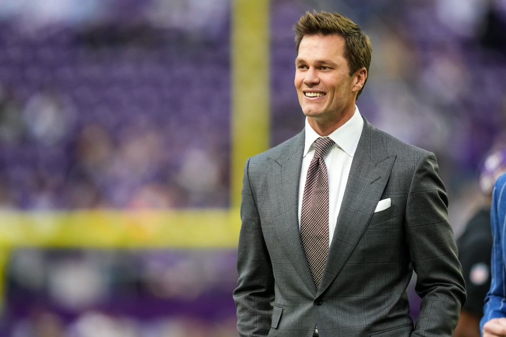 A man in a gray suit smiles at a football game.