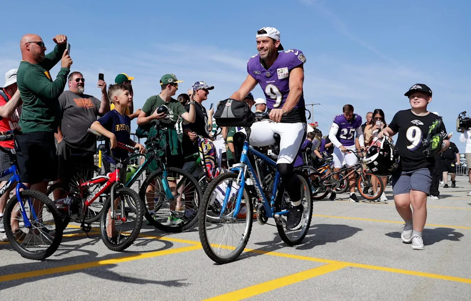 Baltimore Ravens kicker Justin Tucker (9) rides a young fan's bicycle to a joint practice with the Green Bay Packers on Aug. 22, 2024. in Green Bay.