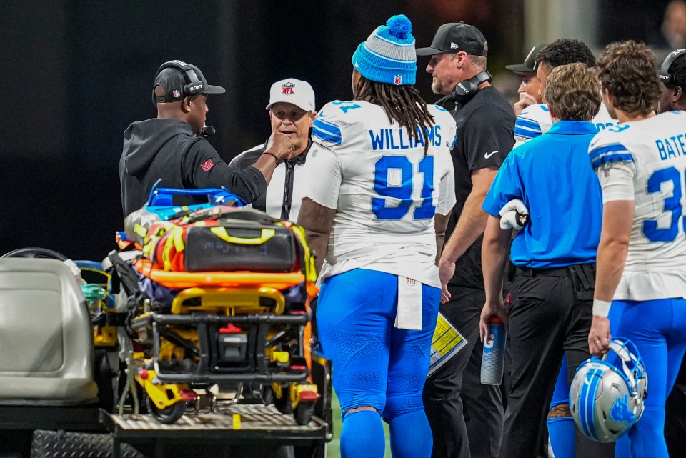 Detroit Lions head coach Dan Campbell and others on the field near a medical cart.