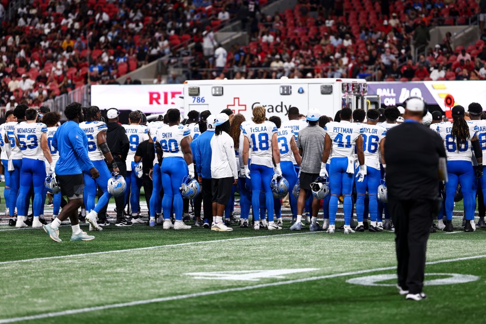 Detroit Lions players huddle near an ambulance.