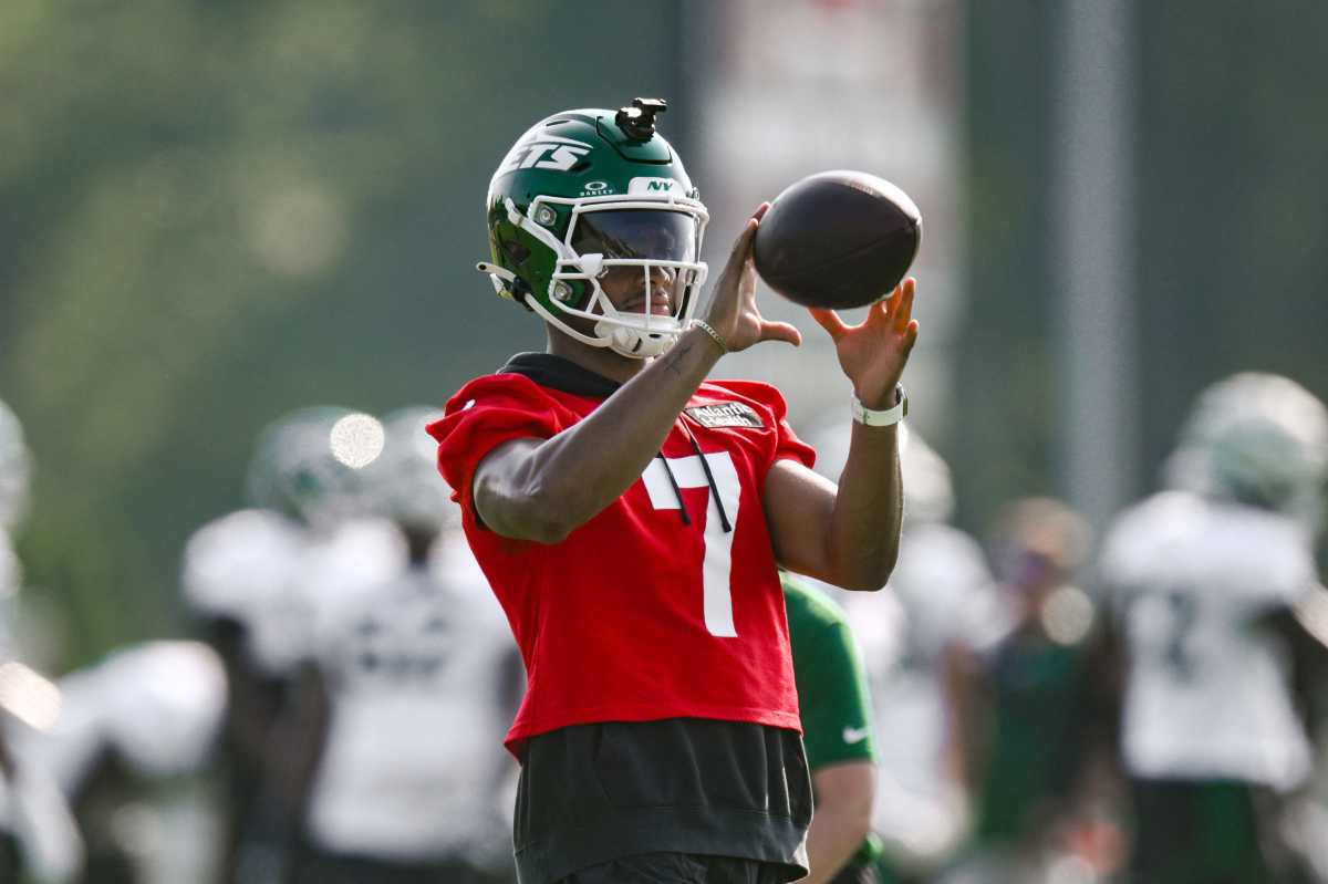 man in red jersey with number 7 on it and green jets helmet holds football, about to throw