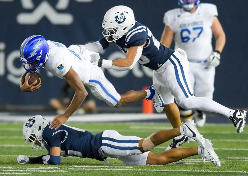 Utah State cornerback D'Angelo Mayes, bottom, and linebacker John Miller tackle Air Force quarterback Josh Johnson (11) during the second half Saturday Sept. 13, 2025, in Logan, Utah. | Eli Lucero/Herald Journal