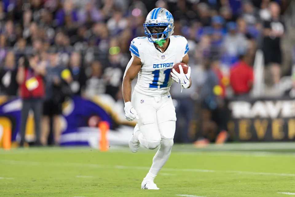 Football player in action wearing a Detroit jersey, holding the ball running on the field during a game