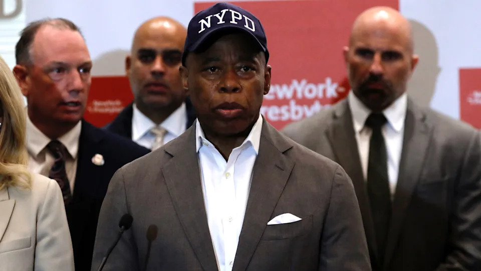 Eric Adams wearing an NYPD cap speaks at a podium, surrounded by four people, in front of a NewYork-Presbyterian backdrop.
