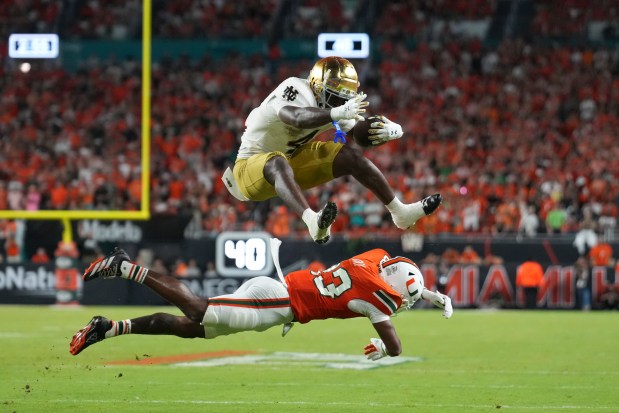 Notre Dame Fighting Irish running back Jeremiyah Love (4) leaps over Miami Hurricanes defensive back Dylan Day (23) during an NCAA football game on Sunday, Aug. 31, 2025 in Miami. (AP Photo/Peter Joneleit)