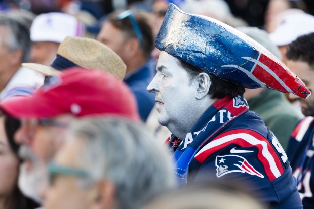 A fan dressed as the Patriots mascot sits among the...