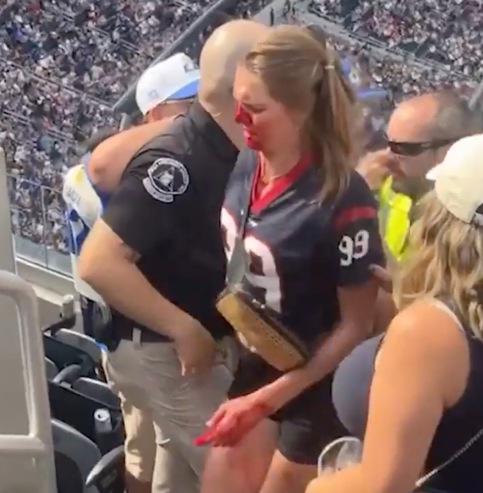 A bleeding woman is being helped by a security guard in a crowded stadium.