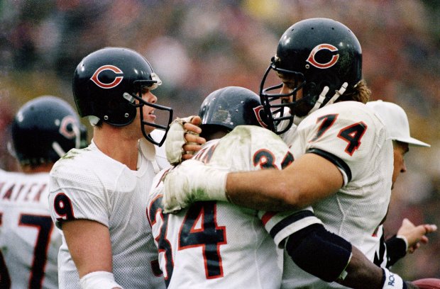 Walter Payton (34), center, ends up in a bear hug from tackle Jim Covert after scoring on a 27-yard run during a 16-10 victory over the Green Bay Packers on Nov. 3, 1985, at Lambeau Field in Green Bay. Quarterback Jim McMahon looks on at left. (Bob Langer/Chicago Tribune)