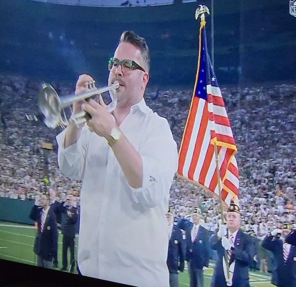 Trumpeter performing at a football game with the American flag.
