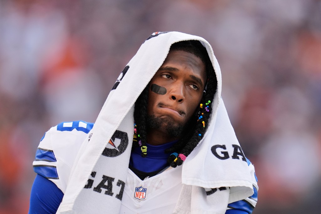 CeeDee Lamb in a white Dallas Cowboys jersey with a towel over his head, walking along the sideline during a game.