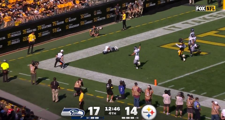 A Seattle Seahawks player celebrating a touchdown while a Pittsburgh Steelers player is on the ground.