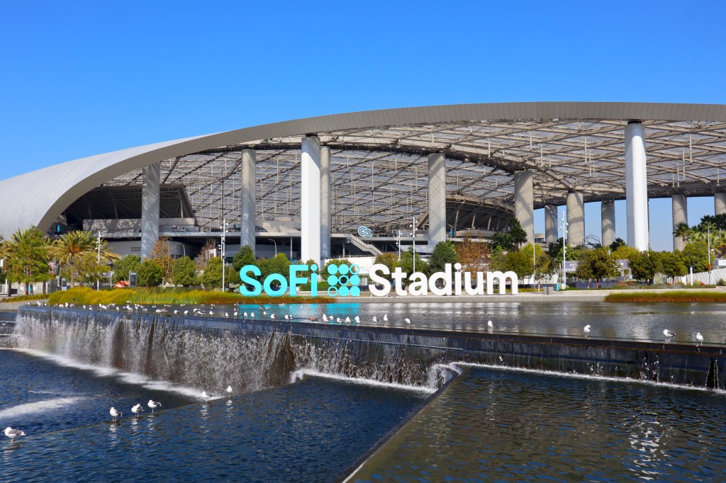 SoFi Stadium exterior with a water feature and "SoFi Stadium" sign in the foreground.