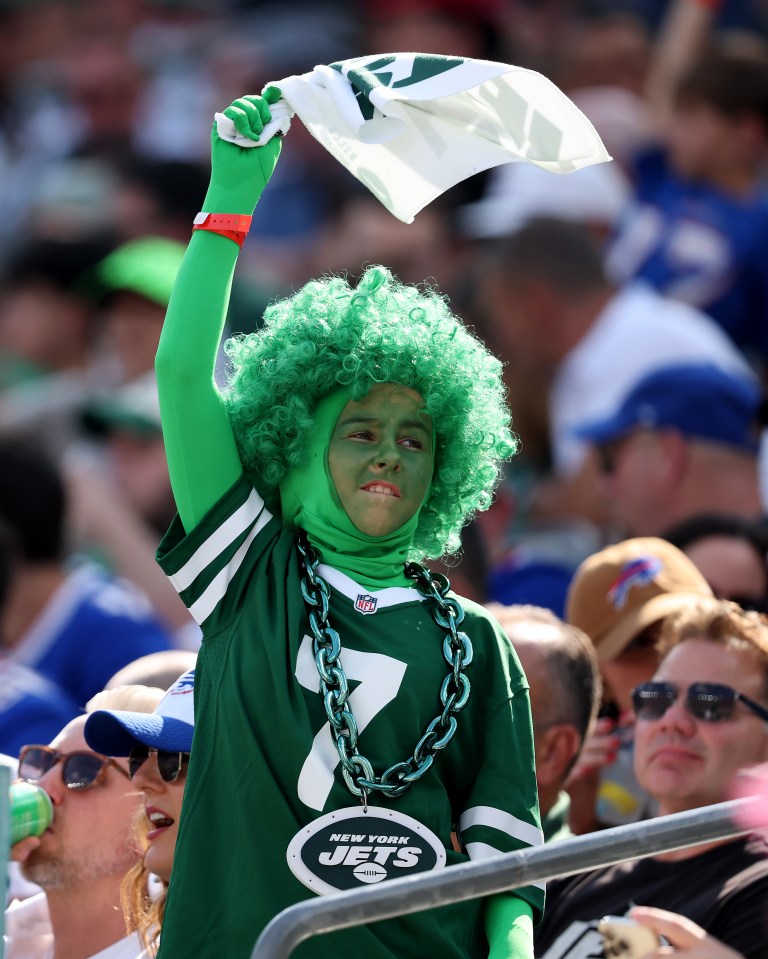 New York Jets fan wearing green face paint, green wig, green uniform, and holding a flag.