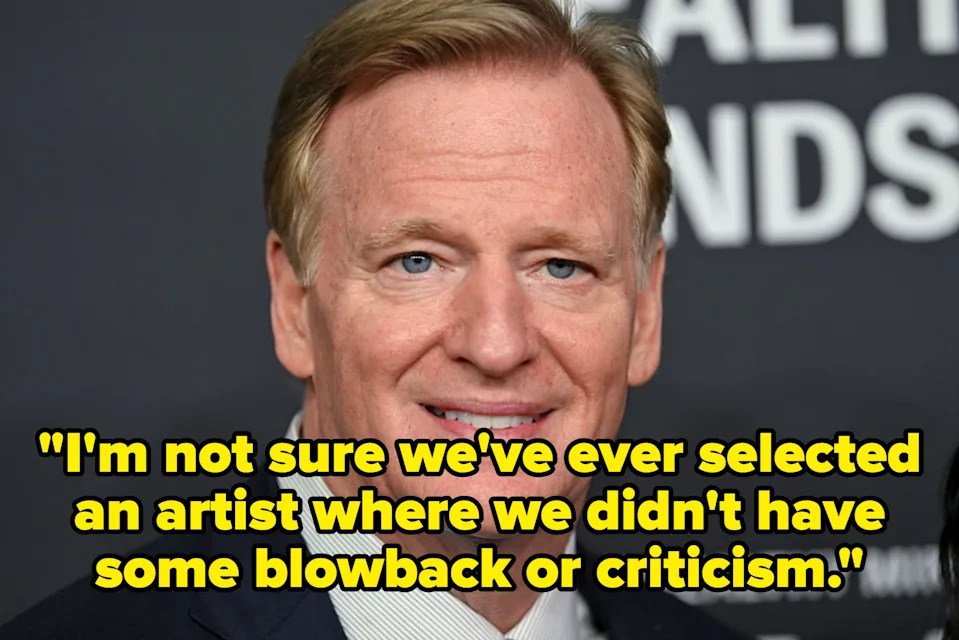 A person in formal attire poses in front of a backdrop with partially visible text at a celebrity event