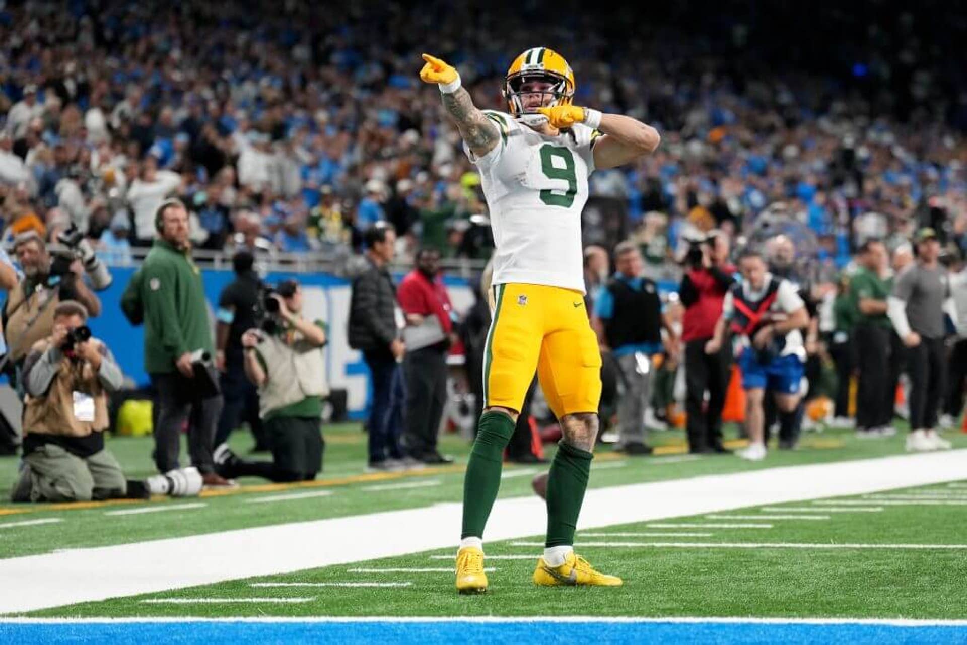 Wearing a white Packers jersey with gold pants and helmet, receiver Christian celebrates after a long catch by striking a pose with his arms pointing off in a downfield direction.