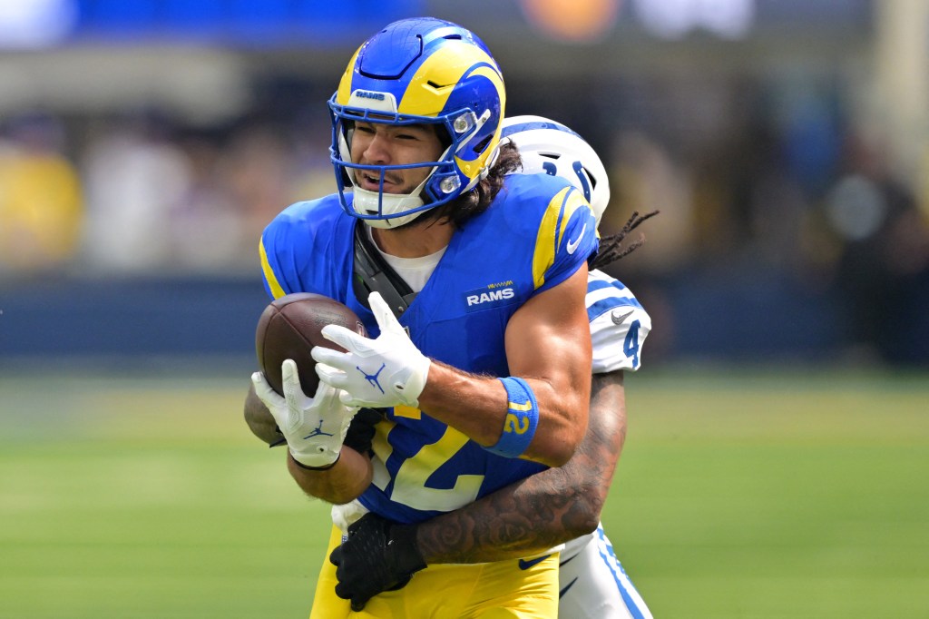 A Rams player in blue and yellow uniform with a football is being tackled by a Colts player in a white uniform.