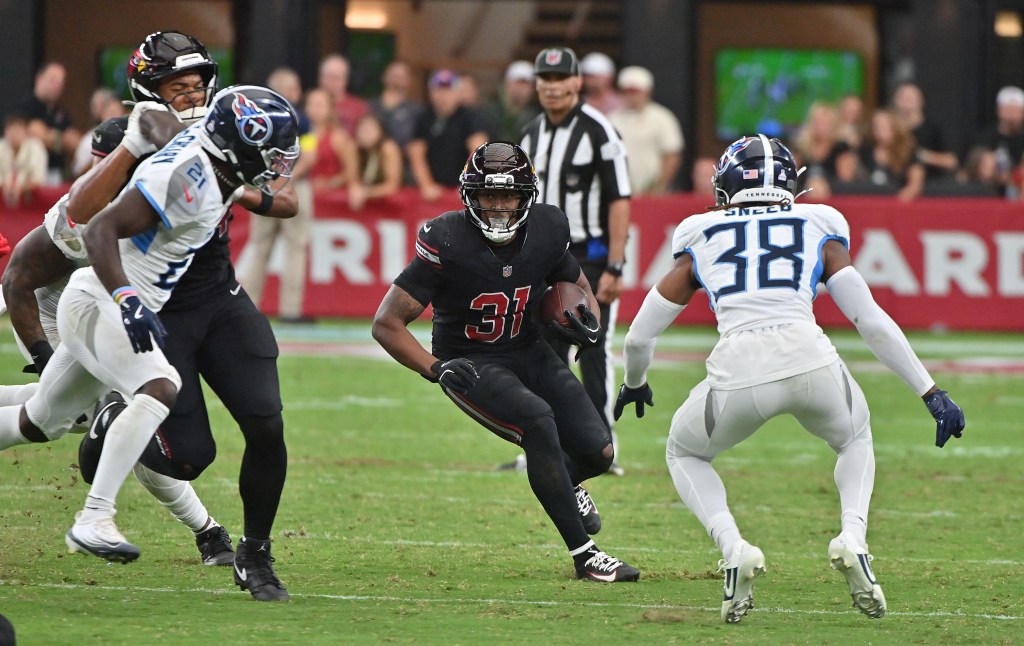 A player in a black uniform with the number 31 holding a football, running past two players in white uniforms.