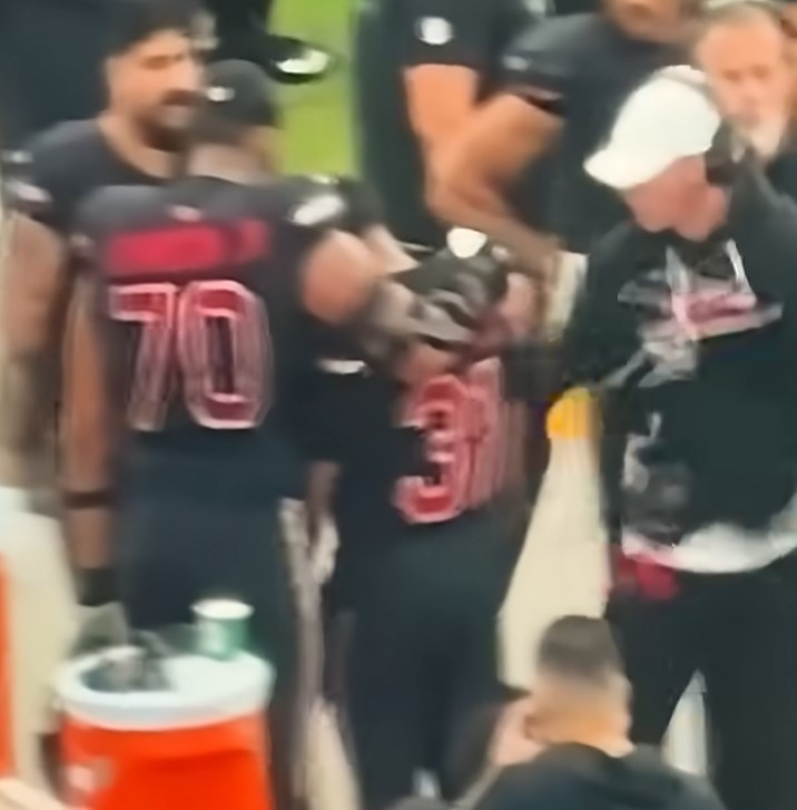Two football players, number 70 and 31, and a coach on the sideline.