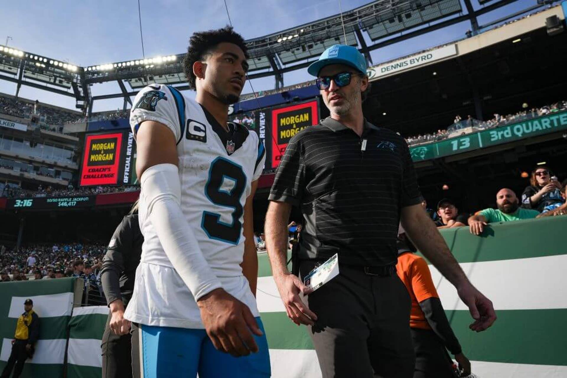 Bryce Young, wearing his white and blue Carolina Panthers (No. 9) jersey, walks off the field with a team official during an NFL game against the New York Jets.