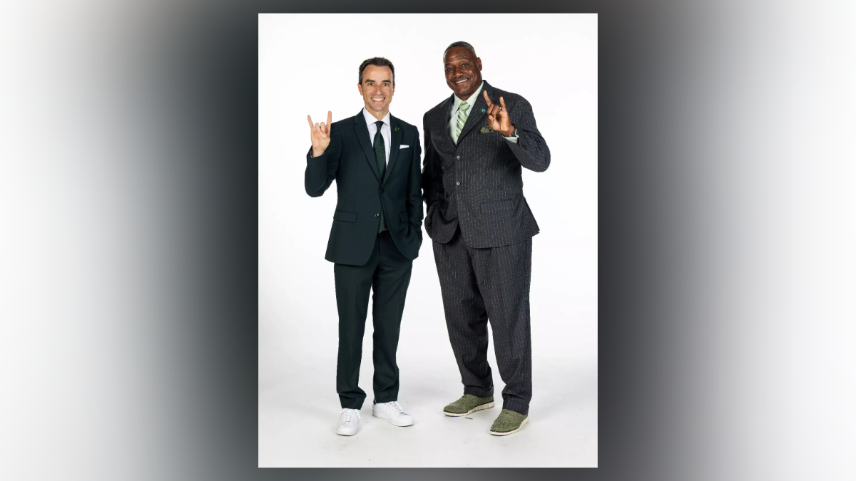 Rob Higgins and Derrick Brooks pose together, both wearing suits and making the USF Bulls hand sign to celebrate Brooks’ new role as chief operating officer of USF Athletics.