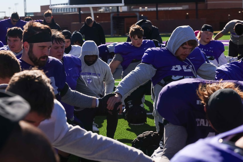 Players bow their heads as Tarleton State Texans head coach Todd Whitten leads them in the...