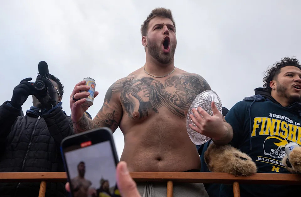 Michiganâ€™s Trevor Keegan holds a beer in one hand and the 2023 National Championship trophy in the other during a parade at the University of Michigan campus in Ann Arbor on Saturday, Jan. 13, 2024.